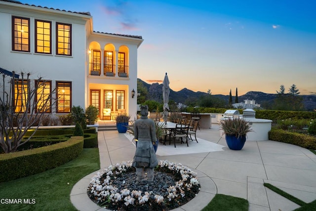 patio terrace at dusk with a mountain view, a balcony, and exterior kitchen