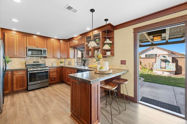 kitchen with appliances with stainless steel finishes, pendant lighting, dark stone countertops, a breakfast bar area, and kitchen peninsula