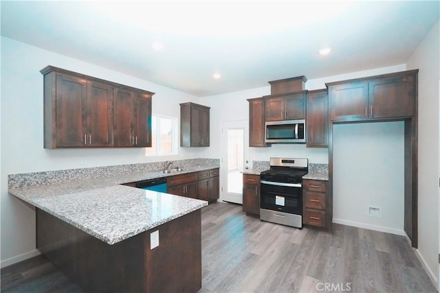 kitchen featuring sink, stainless steel appliances, dark brown cabinetry, light stone counters, and light wood-type flooring