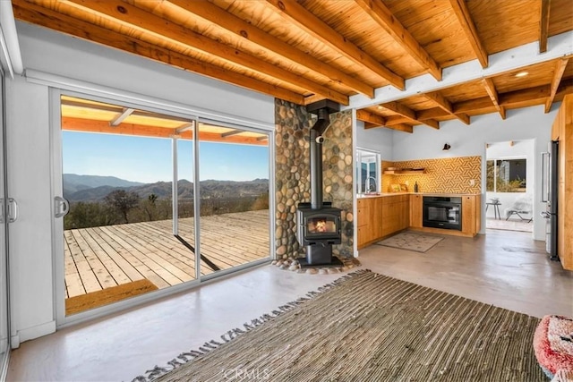 doorway with a mountain view, wooden ceiling, concrete floors, beamed ceiling, and a wood stove