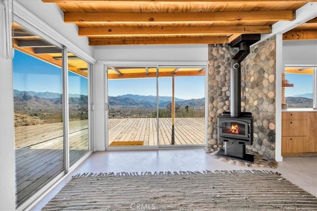 interior space with a mountain view, a wood stove, a wealth of natural light, and wooden ceiling