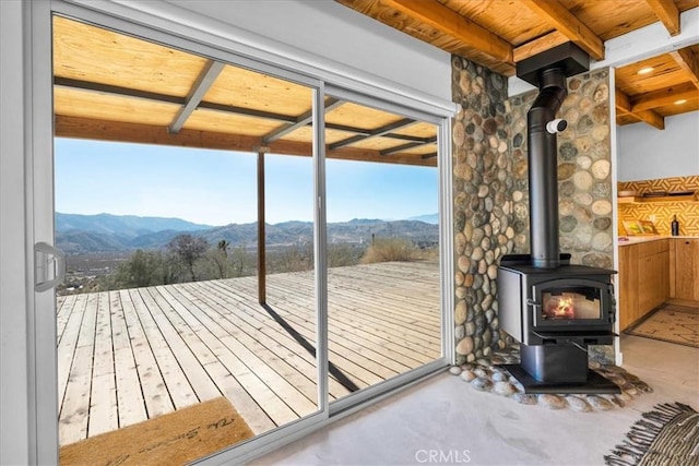 entryway with a mountain view, wooden ceiling, beamed ceiling, and a wood stove