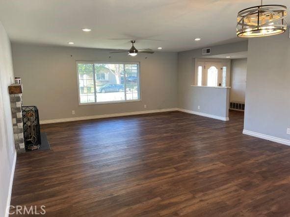 unfurnished living room featuring ceiling fan with notable chandelier and dark hardwood / wood-style floors