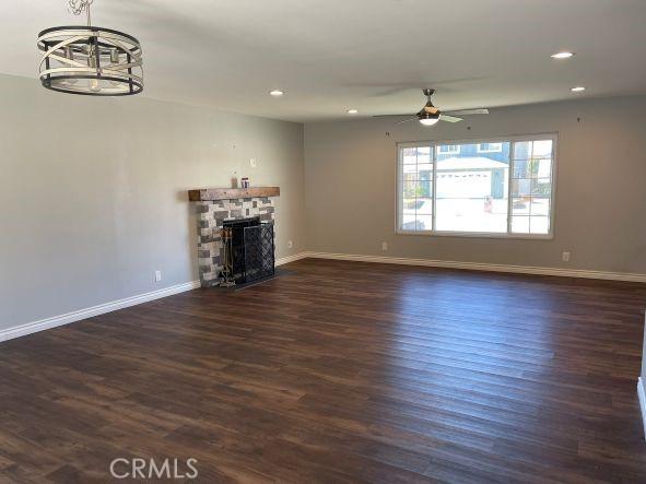 unfurnished living room featuring dark hardwood / wood-style floors, ceiling fan with notable chandelier, and a fireplace