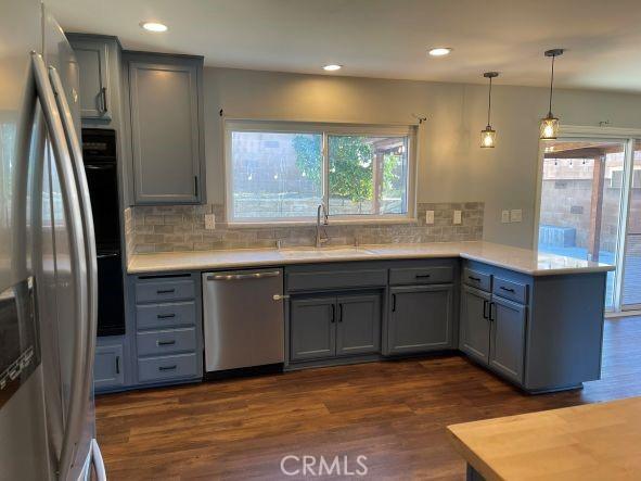 kitchen with sink, dark wood-type flooring, appliances with stainless steel finishes, hanging light fixtures, and kitchen peninsula