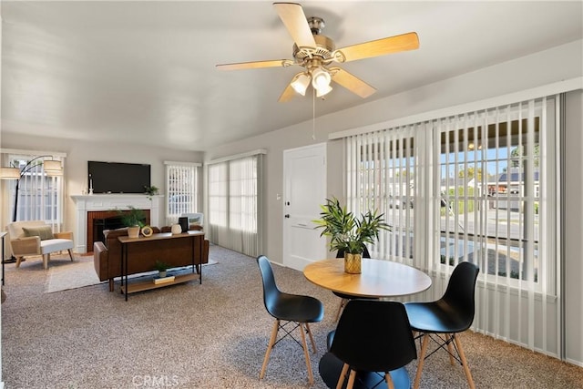 carpeted dining space featuring a brick fireplace and ceiling fan