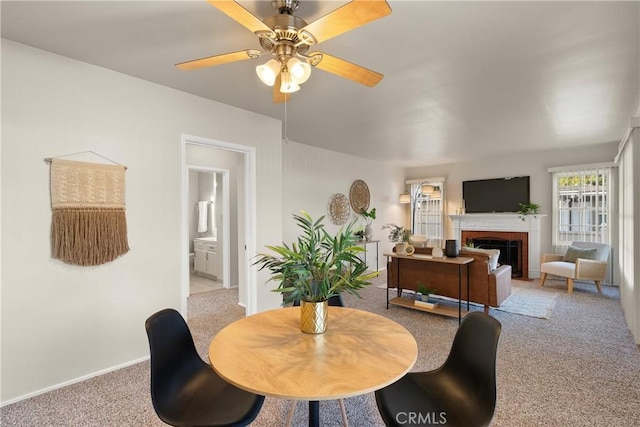 dining space with a fireplace, light colored carpet, and ceiling fan