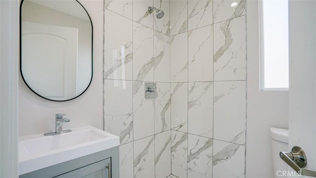 bathroom featuring vanity, a tile shower, and toilet