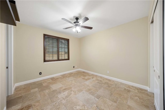 spare room featuring stone finish floor, ceiling fan, and baseboards