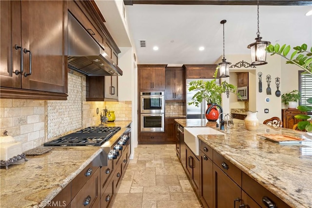 kitchen with under cabinet range hood, stainless steel appliances, a sink, hanging light fixtures, and stone tile flooring