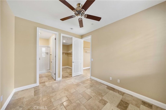 unfurnished bedroom featuring a closet, a walk in closet, stone tile flooring, and baseboards