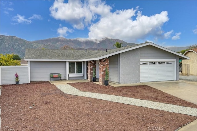 ranch-style house with driveway, a shingled roof, an attached garage, fence, and a mountain view