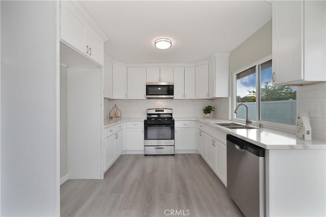 kitchen featuring appliances with stainless steel finishes, a sink, light countertops, light wood-style floors, and backsplash