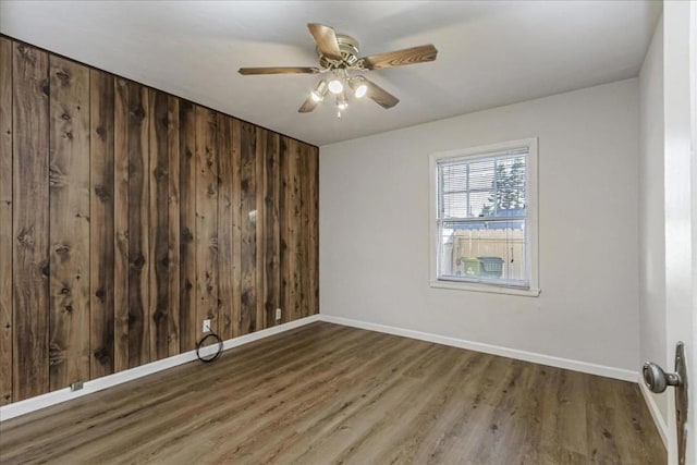 empty room featuring wood-type flooring, ceiling fan, and wood walls