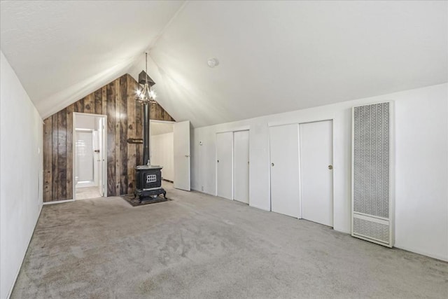 additional living space with lofted ceiling, a wood stove, and light colored carpet