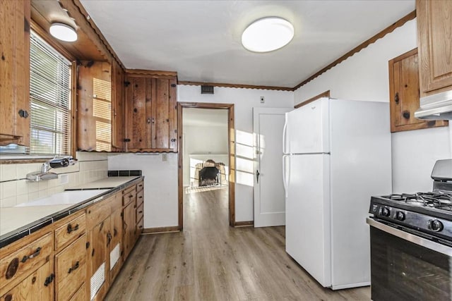 kitchen featuring black gas range oven, sink, decorative backsplash, white fridge, and light hardwood / wood-style flooring