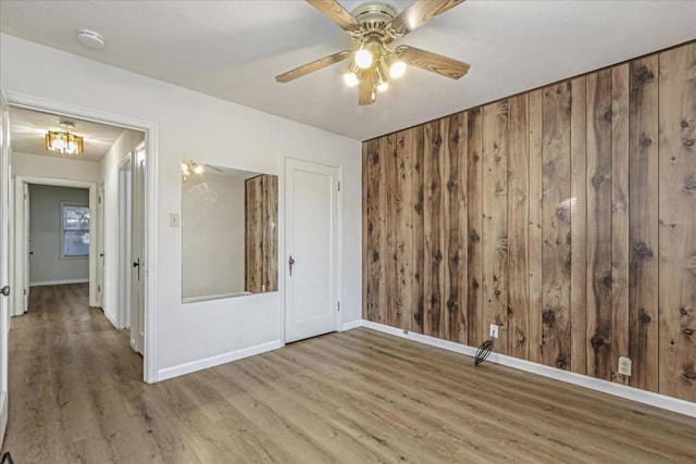 empty room featuring ceiling fan, wooden walls, and hardwood / wood-style floors