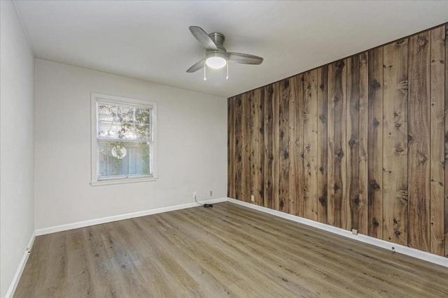 spare room featuring hardwood / wood-style floors, ceiling fan, and wood walls