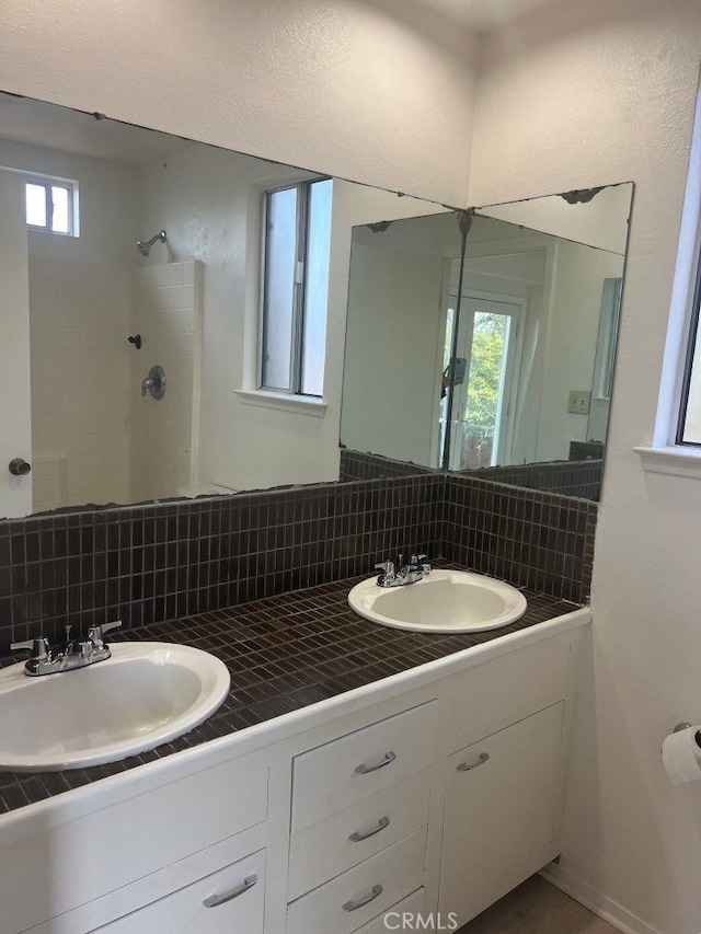 full bath featuring a tile shower, backsplash, a healthy amount of sunlight, and a sink