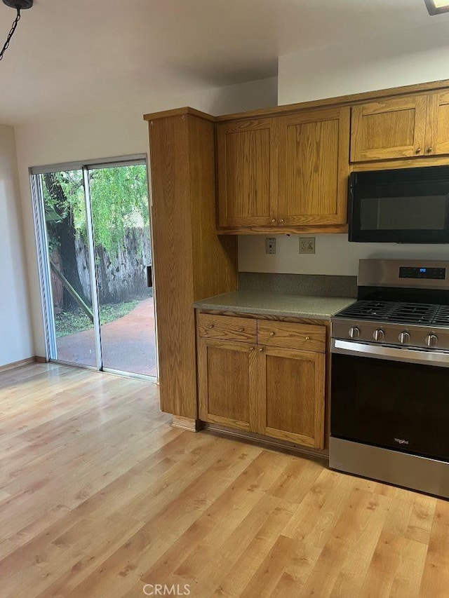 kitchen featuring light wood finished floors, brown cabinets, black microwave, and stainless steel range with gas cooktop