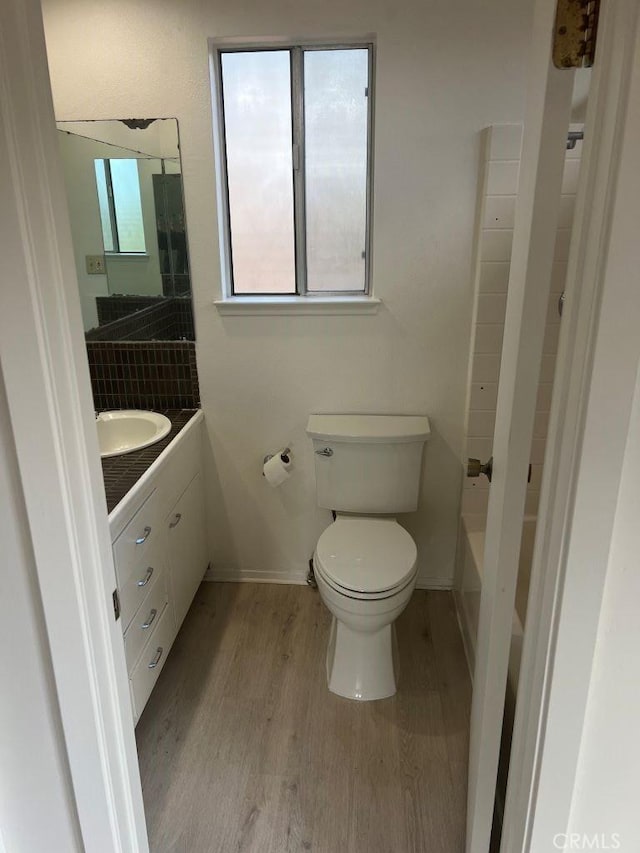 full bath with vanity, wood finished floors, baseboards, toilet, and a bathtub