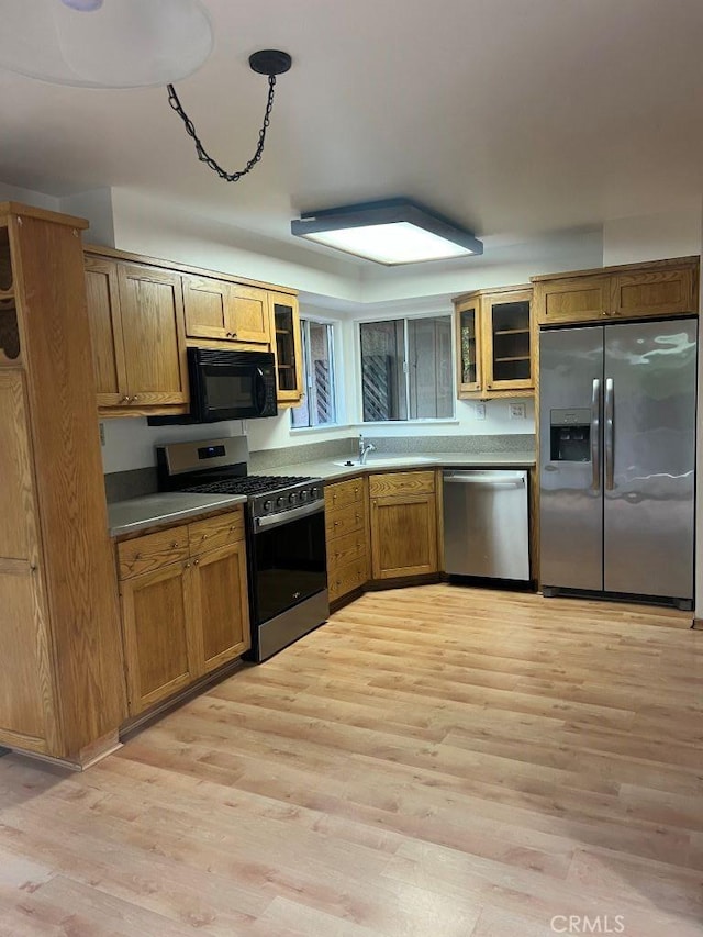 kitchen with glass insert cabinets, brown cabinets, light wood finished floors, and stainless steel appliances