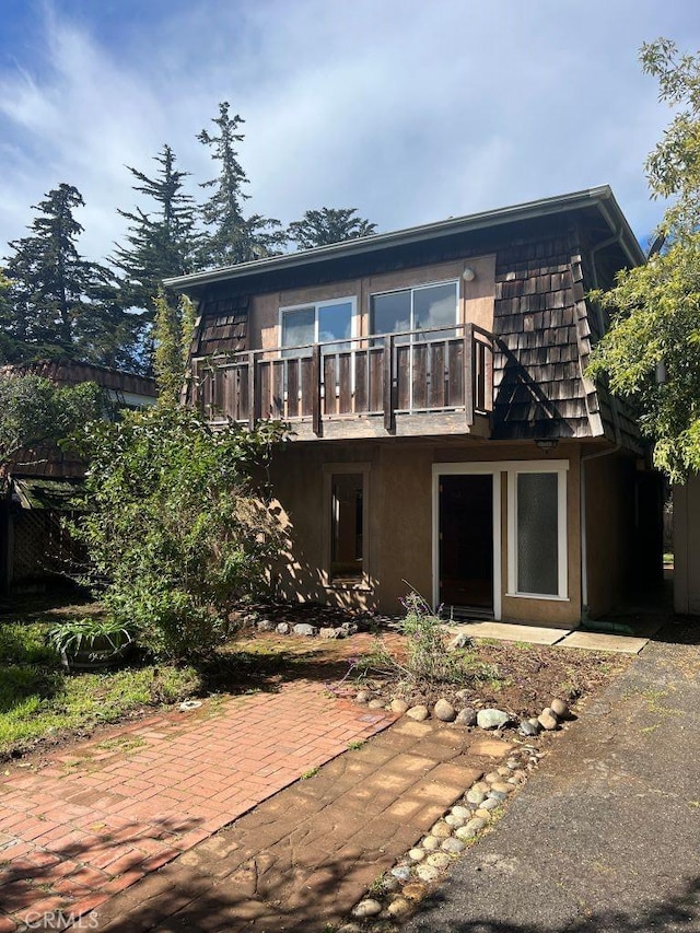 rear view of house featuring mansard roof, a balcony, stucco siding, and a patio area