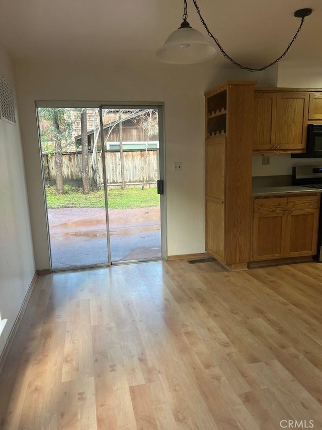 kitchen with light wood finished floors, brown cabinets, stainless steel range oven, and black microwave