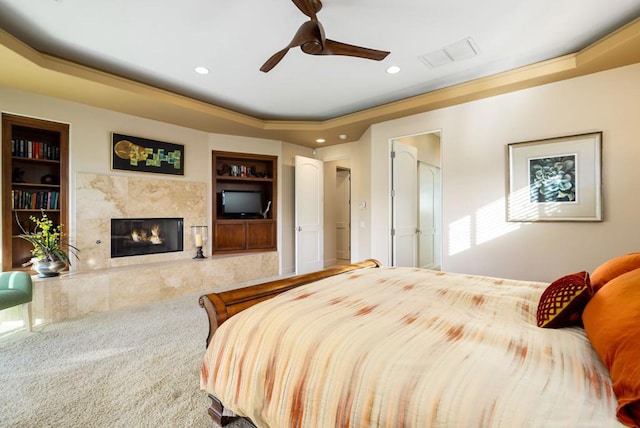 carpeted bedroom featuring a premium fireplace, ceiling fan, and a tray ceiling