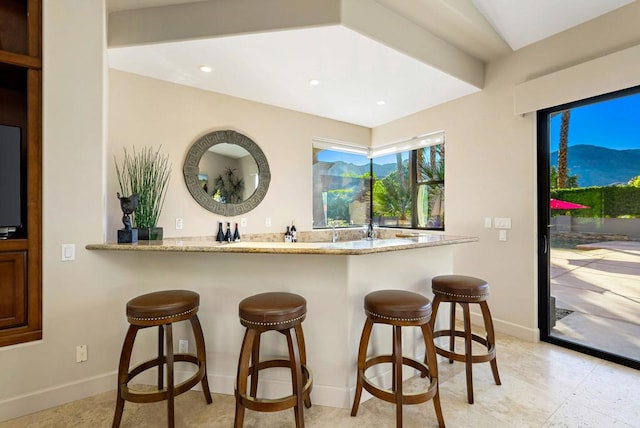 kitchen featuring a mountain view, a breakfast bar, light stone counters, and kitchen peninsula