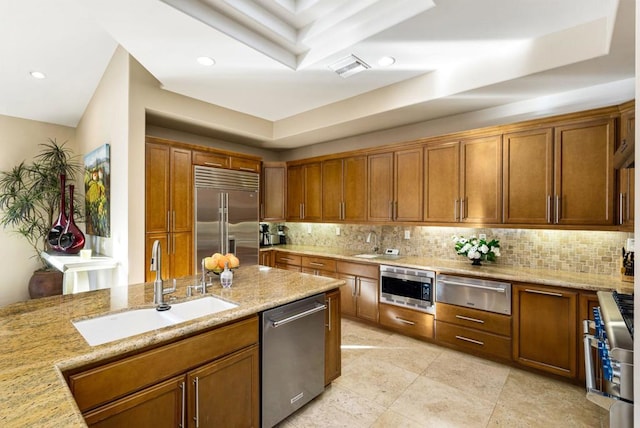 kitchen with tasteful backsplash, built in appliances, light stone countertops, and sink