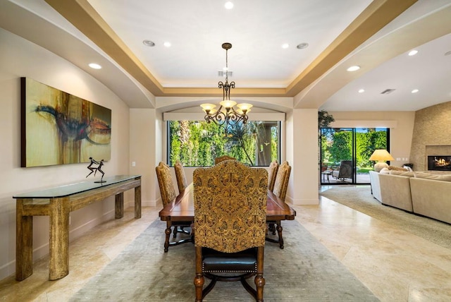 dining space with a notable chandelier, a tray ceiling, and a large fireplace