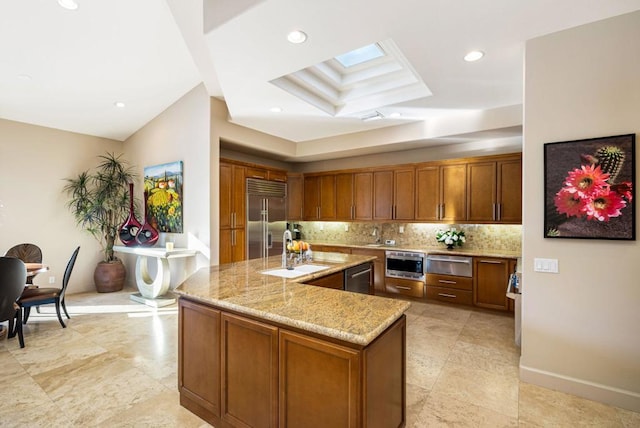 kitchen with sink, stainless steel appliances, tasteful backsplash, light stone countertops, and an island with sink