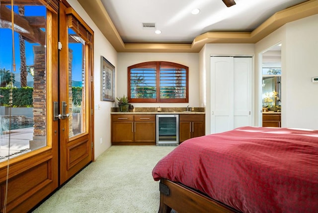 bedroom with access to outside, wet bar, a raised ceiling, light colored carpet, and beverage cooler