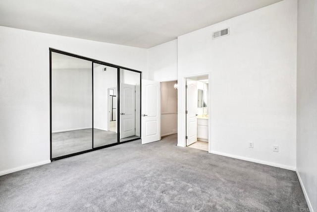 unfurnished bedroom featuring connected bathroom, a closet, a high ceiling, and carpet flooring