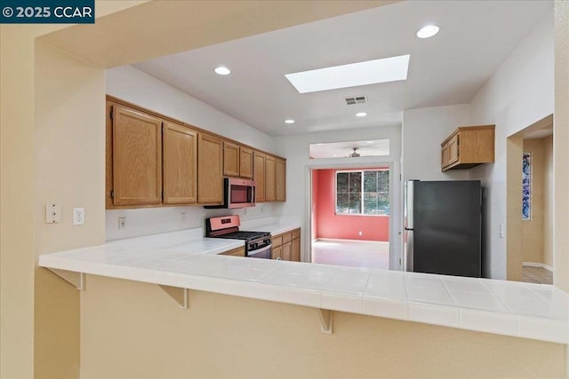 kitchen with a kitchen bar, tile countertops, kitchen peninsula, ceiling fan, and stainless steel appliances