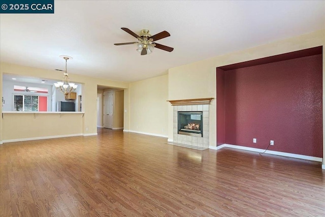 unfurnished living room featuring a tiled fireplace, hardwood / wood-style floors, and ceiling fan with notable chandelier