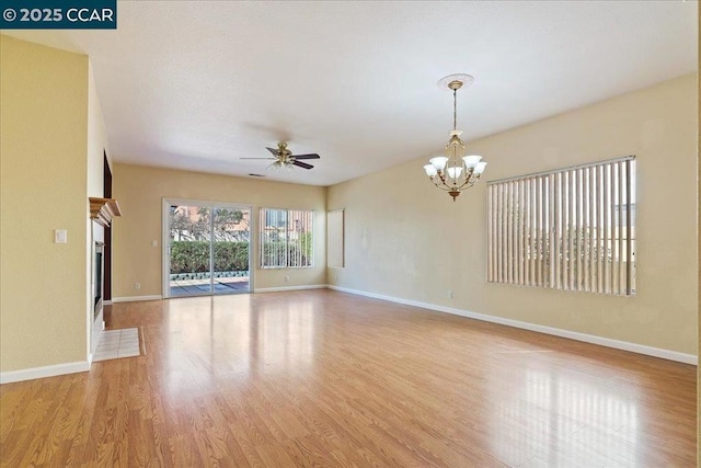 empty room featuring ceiling fan with notable chandelier and light wood-type flooring