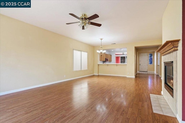 unfurnished living room with wood-type flooring, a fireplace, and ceiling fan with notable chandelier