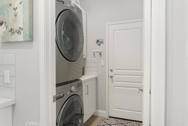 laundry area featuring light wood-type flooring, stacked washer / drying machine, and cabinets