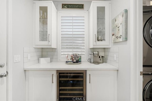 bar featuring wine cooler, stacked washer and dryer, white cabinets, and tasteful backsplash