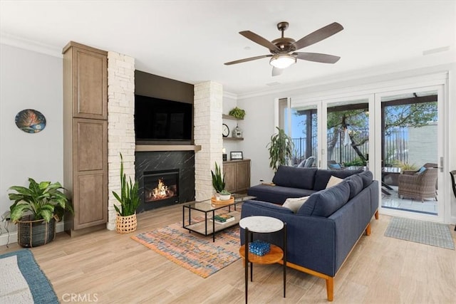 living room with light wood-type flooring, ceiling fan, a large fireplace, and ornamental molding