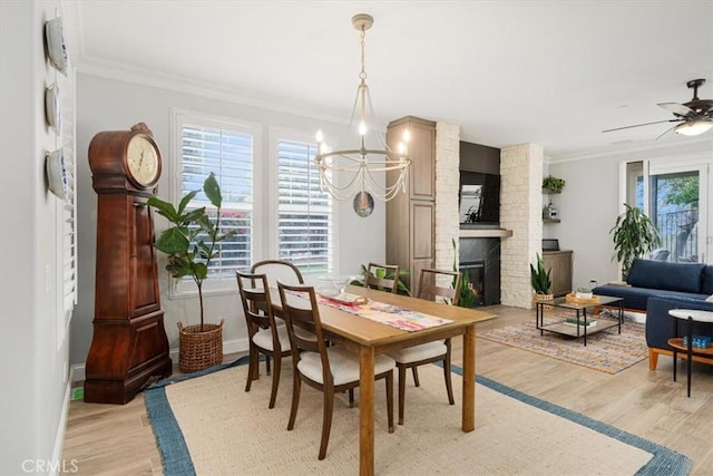 dining area featuring a fireplace, light hardwood / wood-style flooring, crown molding, and ceiling fan with notable chandelier