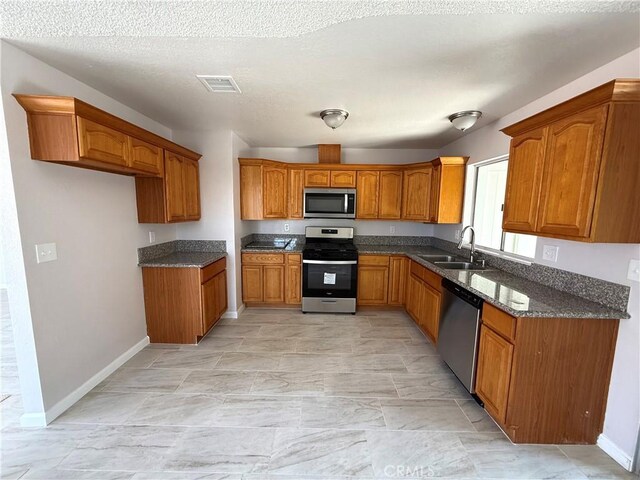 kitchen featuring appliances with stainless steel finishes, sink, a textured ceiling, and dark stone countertops