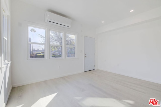 empty room featuring a wall unit AC and light hardwood / wood-style floors