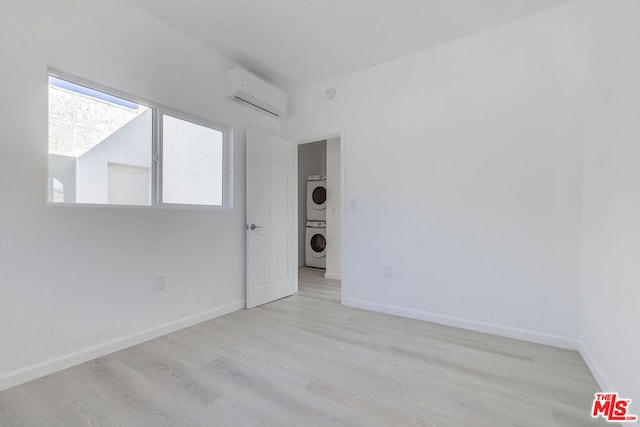 empty room featuring stacked washer / dryer, an AC wall unit, and light wood-type flooring