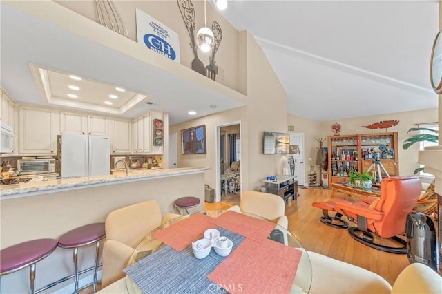 dining space with lofted ceiling, a tray ceiling, light hardwood / wood-style flooring, and a baseboard heating unit