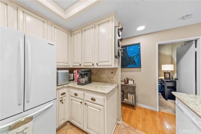 kitchen featuring light wood-type flooring, white refrigerator, light stone countertops, decorative backsplash, and cream cabinetry