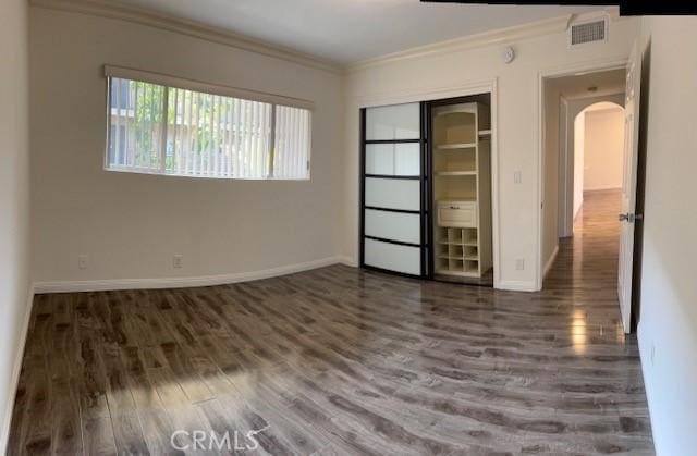 unfurnished bedroom featuring crown molding, dark wood-type flooring, and a closet