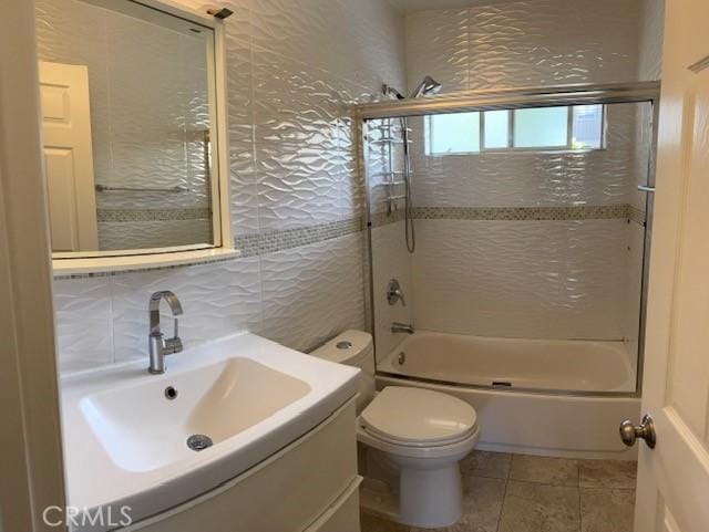 full bathroom featuring combined bath / shower with glass door, tile walls, vanity, tile patterned floors, and toilet